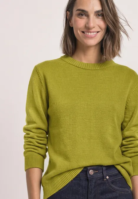 Een vrouw draagt een lichtgroene trui en een spijkerbroek.