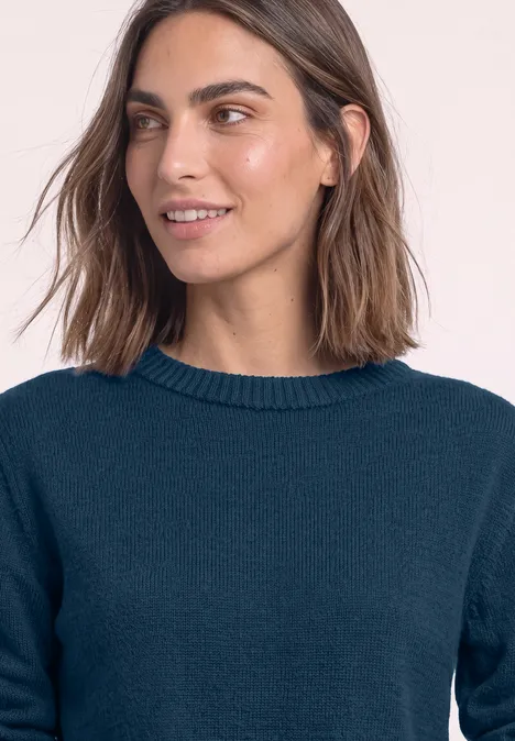 Jonge vrouw met halflang bruin haar en een donkerblauwe trui, lichtjes glimlachend van opzij.
