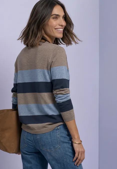 Pullover mit Rundhals und Streifen deep blue Eine lächelnde Frau in gestreiftem Pullover und Jeans, trägt Tasche vor pastellfarbenem Hintergrund.