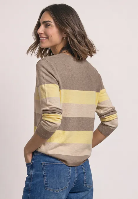 Pullover mit Rundhals und Streifen sanded amber mel. Frau mit schulterlangem Haar im gelb-beige gestreiften Pullover und Jeans schaut lächelnd über die Schulter.