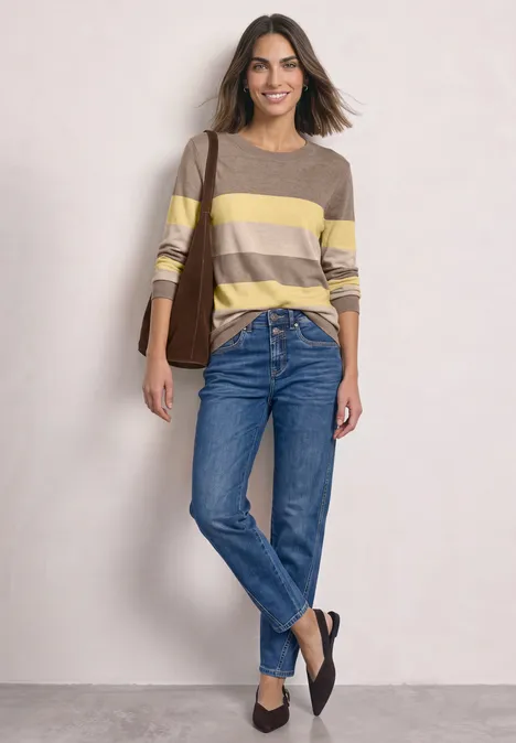 Pullover mit Rundhals und Streifen sanded amber mel. Frau in gestreiftem gelb-beige Pullover, blauen Jeans und schwarzen Schuhen vor hellem Hintergrund.