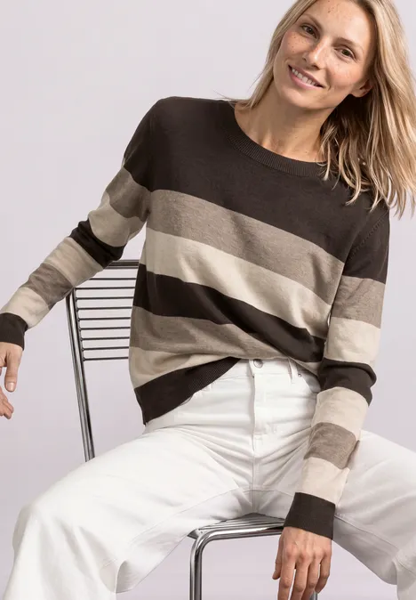 Pullover mit Rundhals und Streifen black coffee Frau sitzt lässig auf einem Stuhl, trägt gestreiften Pullover in Braun- und Beigetönen und weiße Hosen.