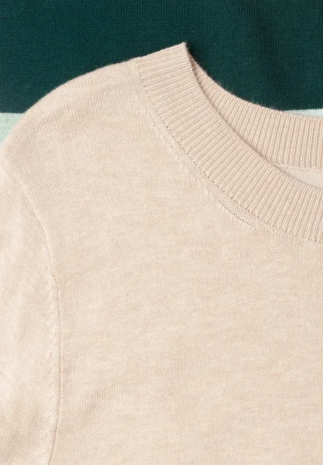 Beige trui met ronde hals op een donkergroene ondergrond.