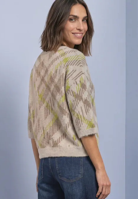 Femme portant un pull beige à motifs, regard par-dessus l'épaule.
