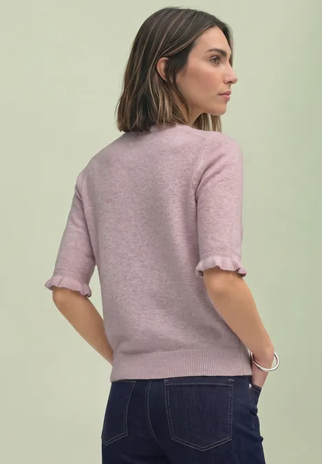 Frau mit halblangen braunen Haaren steht Rücken zur Kamera, trägt pinken Pullover und Jeans.