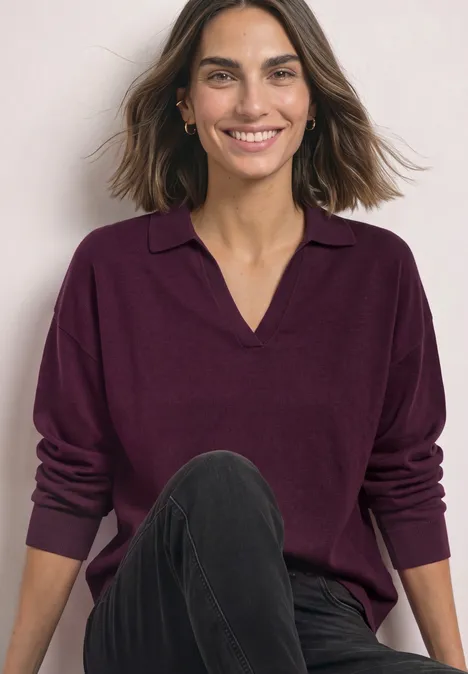 Langarm Pullover mit Polokragen berry maroon Frau lächelt, trägt dunkelvioletten Pullover mit V-Ausschnitt und Kragen sowie schwarze Jeans.
