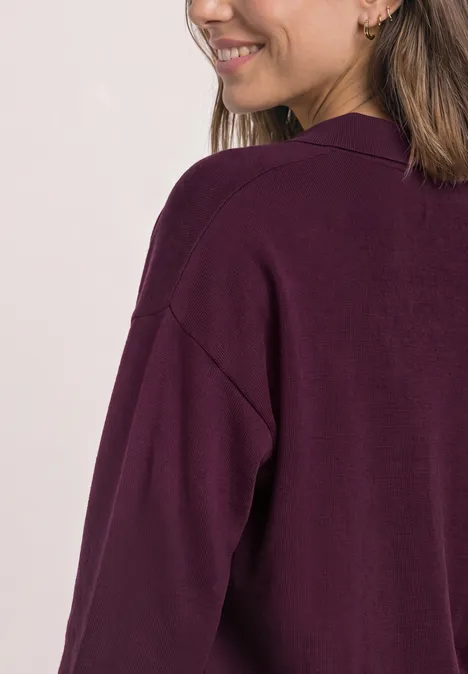 Langarm Pullover mit Polokragen berry maroon Frau in lockerem, dunkelviolettem Cardigan, von hinten/seitlich mit Lächeln und sichtbarer Schulterpartie.