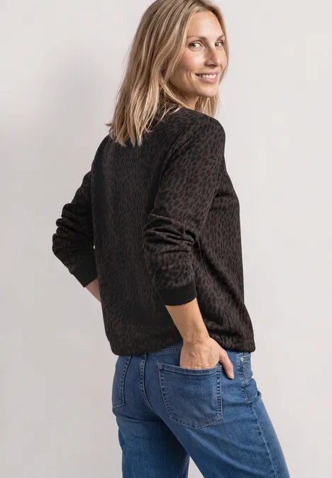 Sweatshirt mit Rundhals und Print molten earth Frau in braunem Pullover und blauen Jeans, seitlich stehend mit Händen in den Taschen, lächelnd.