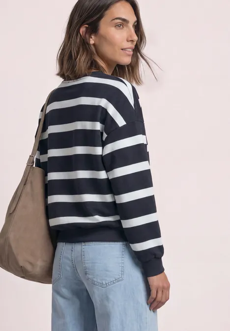 Eine Frau in maritim gestreiftem Pullover und Jeans trägt eine Umhängetasche, seitliche Ansicht.