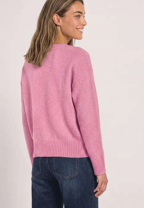 Junge Frau von hinten in rosa Pullover und Jeans, im Profil lächelnd.