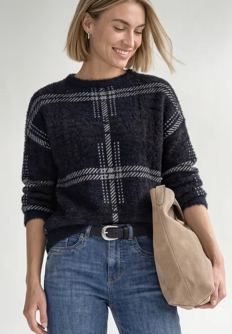 Langarm Pullover mit Karomuster indigo night Eine lächelnde Frau mit blondem Haar trägt einen karierten Pullover, blaue Jeans und hält eine Tasche.