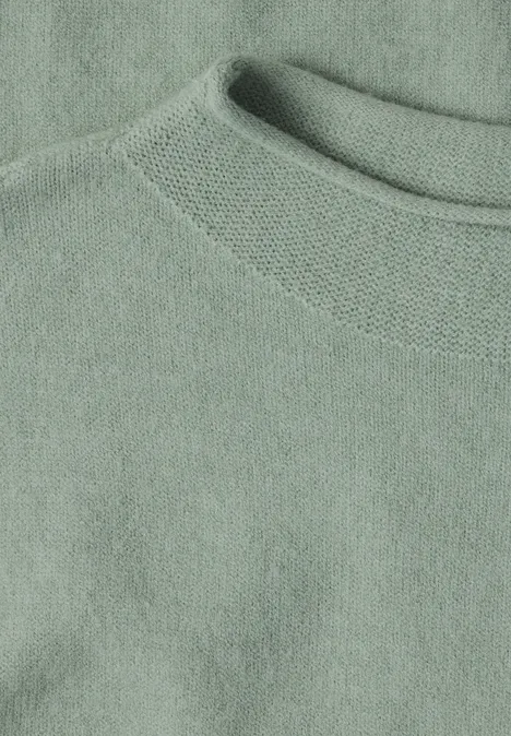 Close-up van een lichtgroene trui/sweater met ronde hals van zachte stof.