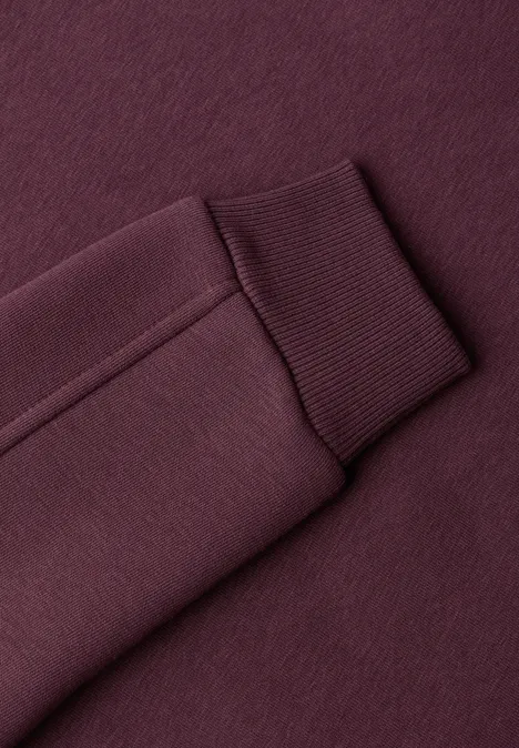 Nahaufnahme eines burgunderfarbenen Sweatshirt-Ärmels mit Rippenbündchen.