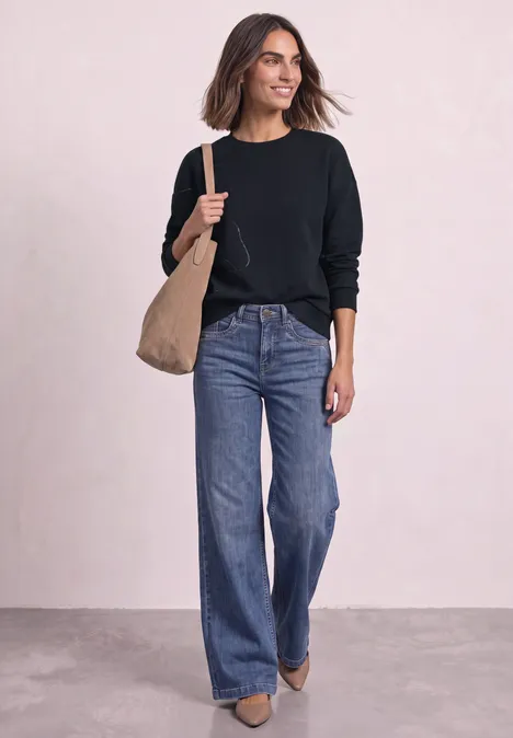 Frau in schwarzem Pullover und weiten Jeans trägt große beige Tasche