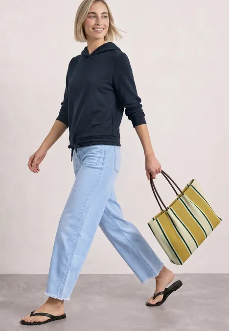 Frau in lässigem Hoodie, Jeans und Flip-Flops trägt gestreifte Tasche