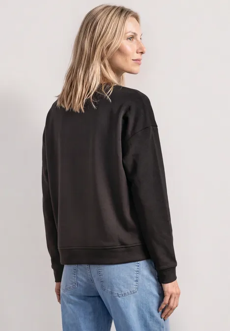 Sweatshirt met lange mouwen en Artwork black coffee Frau in schwarzem Pullover und blauen Jeans, von hinten fotografiert.