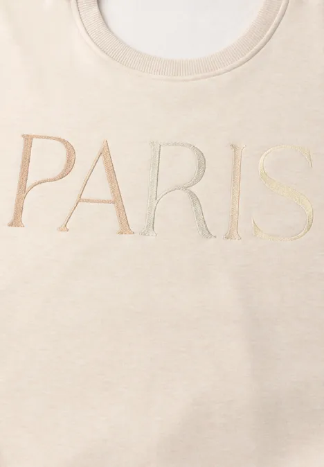 Beiges T-Shirt mit dem Schriftzug PARIS in großen, eleganten Buchstaben.