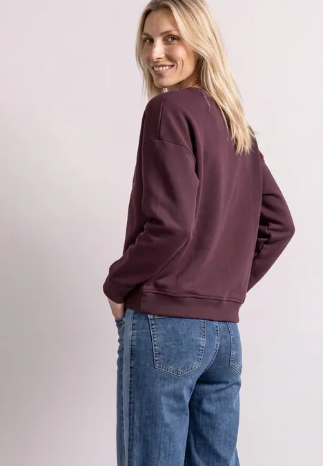 Frau in violettem Pullover und Jeans dreht sich um und lächelt zurück.
