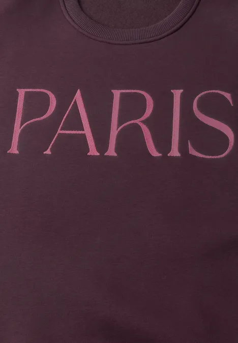 Nahaufnahme eines dunkelroten Sweatshirts mit dem Schriftzug 'PARIS' in großen rosa Buchstaben.