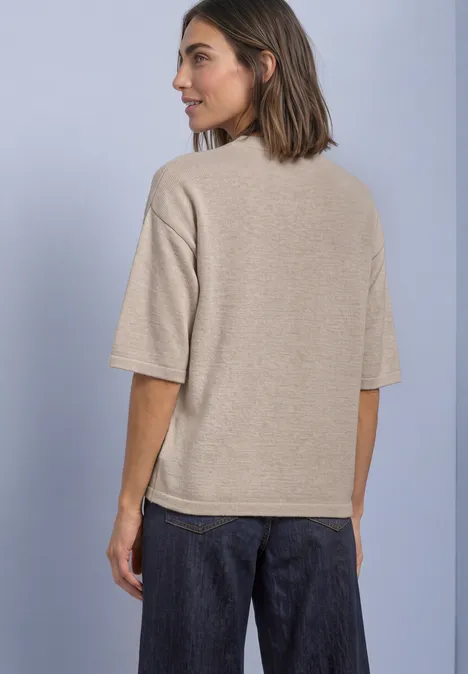 Vrouw van achteren in beige T-shirt met korte mouwen en donkere jeans voor lichte achtergrond.