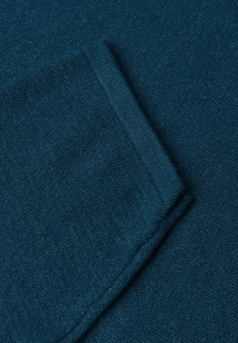 Close-up van een donkerturquoise gebreide stof met een opgestikte zak.