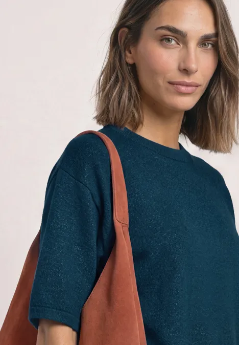 Vrouw met halflang haar in een donkerblauw truitje met korte mouwen en een bruine leren tas.