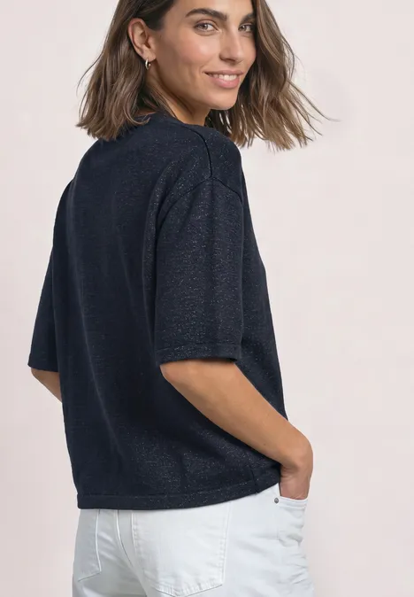 Vrouw in profiel met donkerblauw kort mouw shirt en witte broek, handen in de zakken