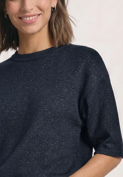 Vrouw met donkerblauwe glittertrui met korte mouwen en ronde hals, zichtbaar lichte glimlach