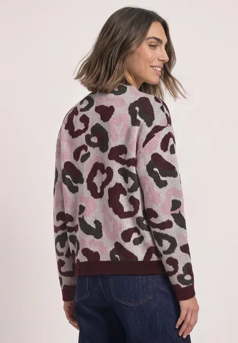 Femme porte un pull élégant à motif léopard rose et marron, associé à un jean.