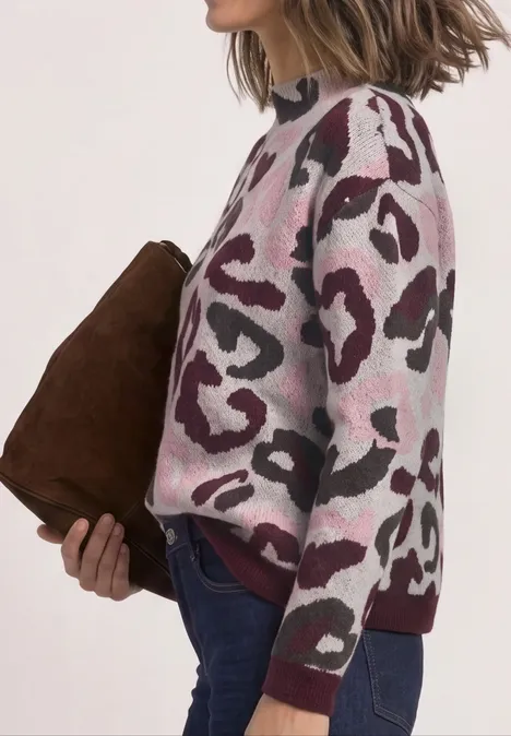 Vue latérale d'une personne portant un pull léopard rose et blanc, un jean et tenant une pochette marron.