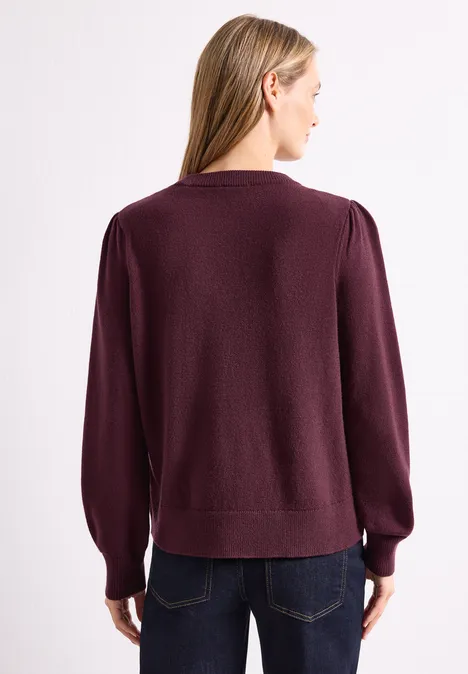 Pull avec inscription brodée rustic rouge Frau von hinten in dunkelviolettem Langarmpullover mit Ballonärmeln und Jeans.