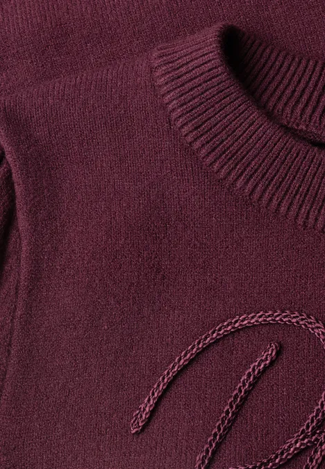 Pull avec inscription brodée rustic rouge Nahaufnahme eines dunkelroten Strickpullovers mit Rundhalsausschnitt und feiner Textur.