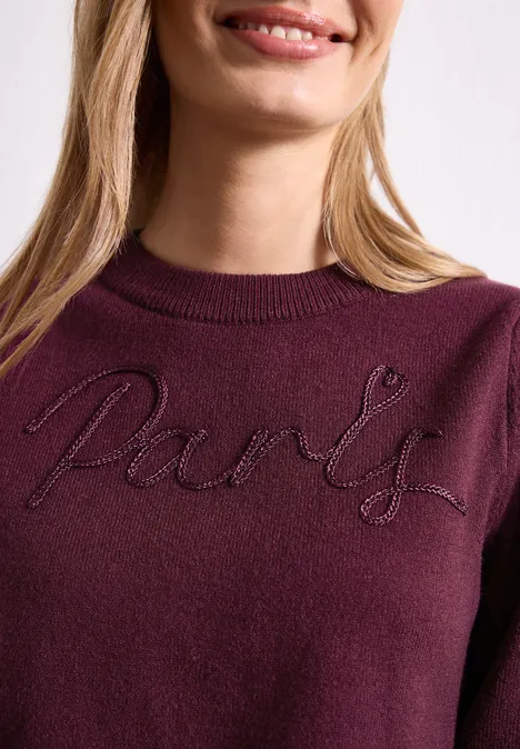Pull avec inscription brodée rustic rouge Frau in bordeauxrotem Pullover mit gesticktem Schriftzug 'Paris'.