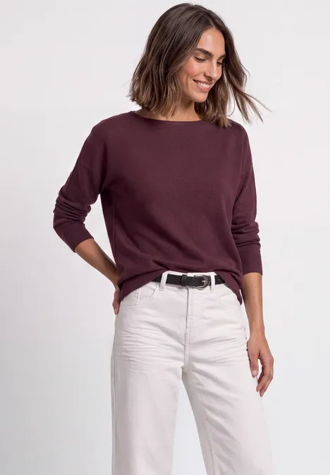 Dolman-trui met boothals rustic rouge Vrouw lacht in een bordeauxrode trui en lichte jeans, ontspannen houding.