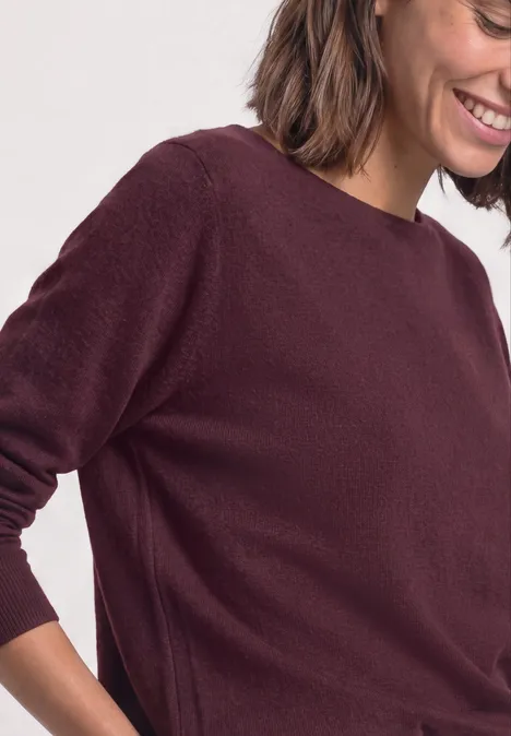Dolman-trui met boothals rustic rouge Een glimlachende vrouw draagt een bordeauxrode trui, deels in profiel.