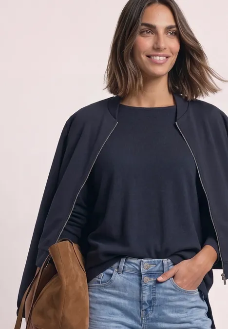 Sweter z rękawami typu dolman i dekoltem w kształcie łódki darkest blue Uśmiechnięta kobieta ma na sobie ciemnoniebieski sweter, marynarkę na ramionach i dżinsy.