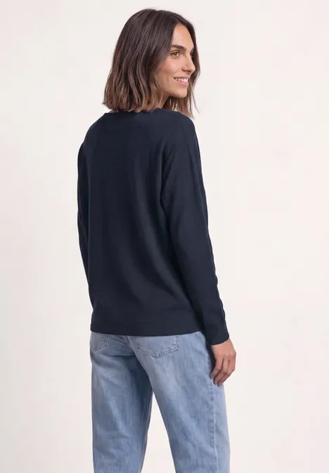Sweter z rękawami typu dolman i dekoltem w kształcie łódki darkest blue Kobieta w granatowym swetrze i dżinsach, bokiem, uśmiechając się, patrzy przez ramię.