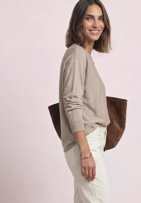 Sweter z rękawami typu dolman i dekoltem w kształcie łódki clay sand mel. Kobieta w beżowym swetrze i białych spodniach, z dużą brązową torbą, uśmiechnięta.