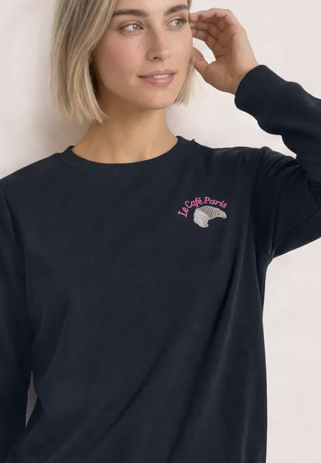 Sweatshirt met ronde hals en borduursel darkest blue Frau mit kurzem blondem Haar in schwarzem Sweatshirt mit kleinem pink-grauen Logo auf der Brust.