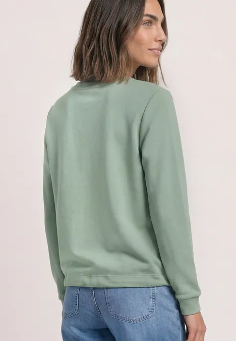 Sweatshirt met ronde hals en borduursel eucalyptus green Frau von hinten in grünem Sweatshirt und blauer Jeans vor neutralem Hintergrund.