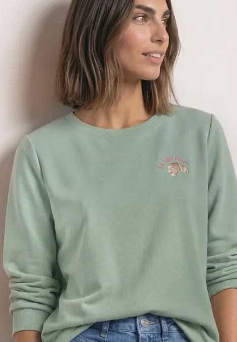 Sweatshirt met ronde hals en borduursel eucalyptus green Frau trägt mintgrünes Sweatshirt mit dezentem Motiv und Jeans, blickt seitlich.