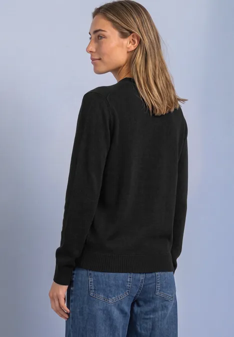 Pullover in Unifarbe mit Rundhals Black Frau steht seitlich vor hellem Hintergrund, trägt schwarzen Pullover und blaue Jeans.