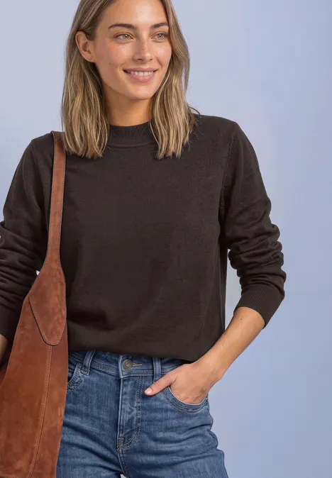 Pullover in Unifarbe mit Rundhals black coffee Frau mit dunkelbraunem Pullover, Jeans und brauner Ledertasche lächelt vor hellem Hintergrund.