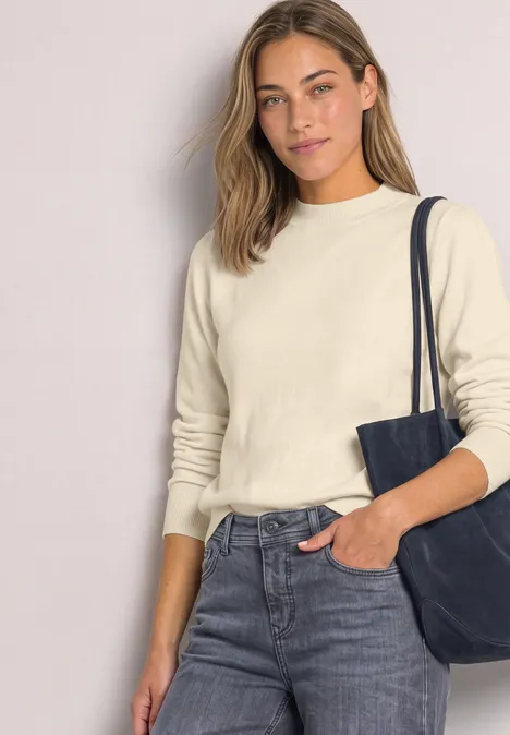 Pullover in Unifarbe mit Rundhals pure beige Frau in Jeans und beigem Pullover mit schwarzer Schultertasche und einer Hand in der Hosentasche.