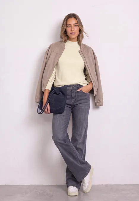 Pullover in Unifarbe mit Rundhals pure beige Eine Frau in beige Bomberjacke, cremefarbenem Pullover, grauen Jeans und weißen Sneakern lehnt an weißer Wand.