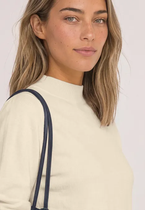 Pullover in Unifarbe mit Rundhals pure beige Frau mit hellbeigem Pullover und dunkelblauer Umhängetasche schaut direkt in die Kamera.