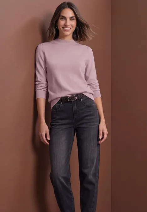 Pullover in Unifarbe mit Rundhals quiet rose Frau im rosafarbenen Pullover und dunklen Jeans steht vor braunem Hintergrund, lächelnd, Hände locker an den Seiten.