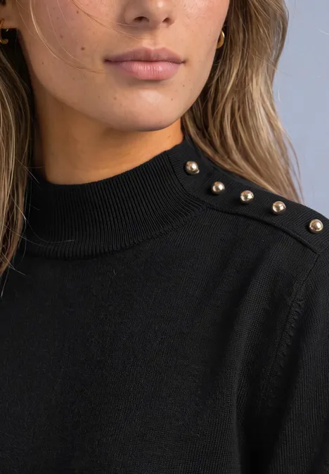 Nahaufnahme einer Frau im schwarzen Pullover mit goldenen Nieten auf der Schulter.