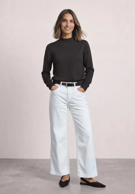Langarm Pullover mit Turtle Neck und Raffung black coffee Frau in weitem weißen Jeans, schwarzem Oberteil, Gürtel und Ballerinas, lächelnd vor neutralem Hintergrund.