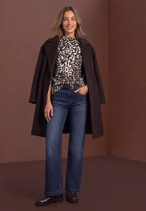 Trui met col en luipaardprint black coffee Vrouw met donkerbruine jas over luipaardblouse, high-waist jeans en bruine schoenen tegen bruine achtergrond.